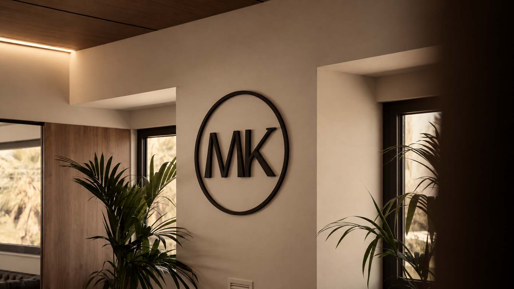 Logotipo MK en la pared de la oficina, entre plantas y ventanas